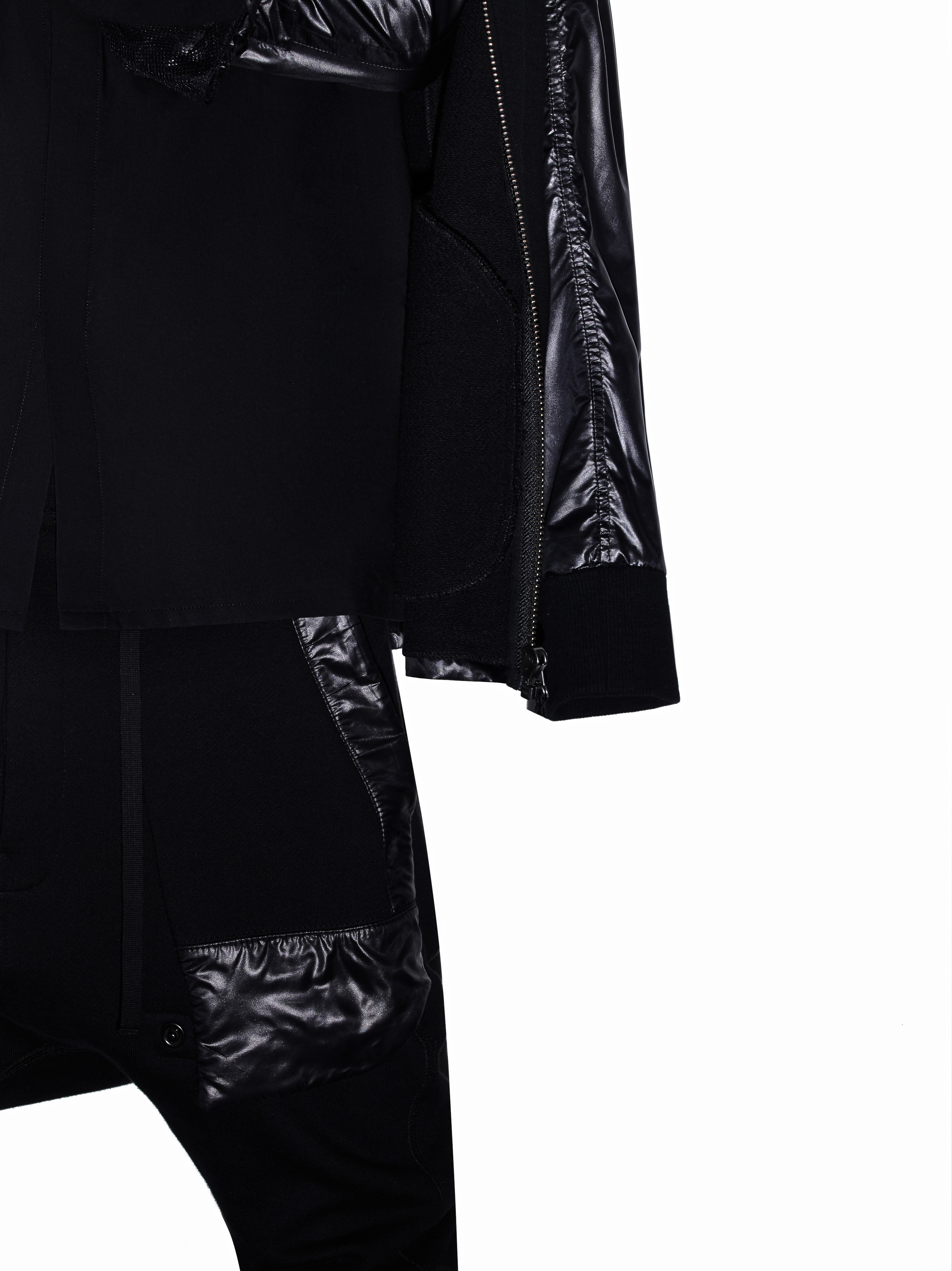 Close-up shot of a black jacket and pants with shiny accents, featuring a modern and sleek fashion design against a white background.