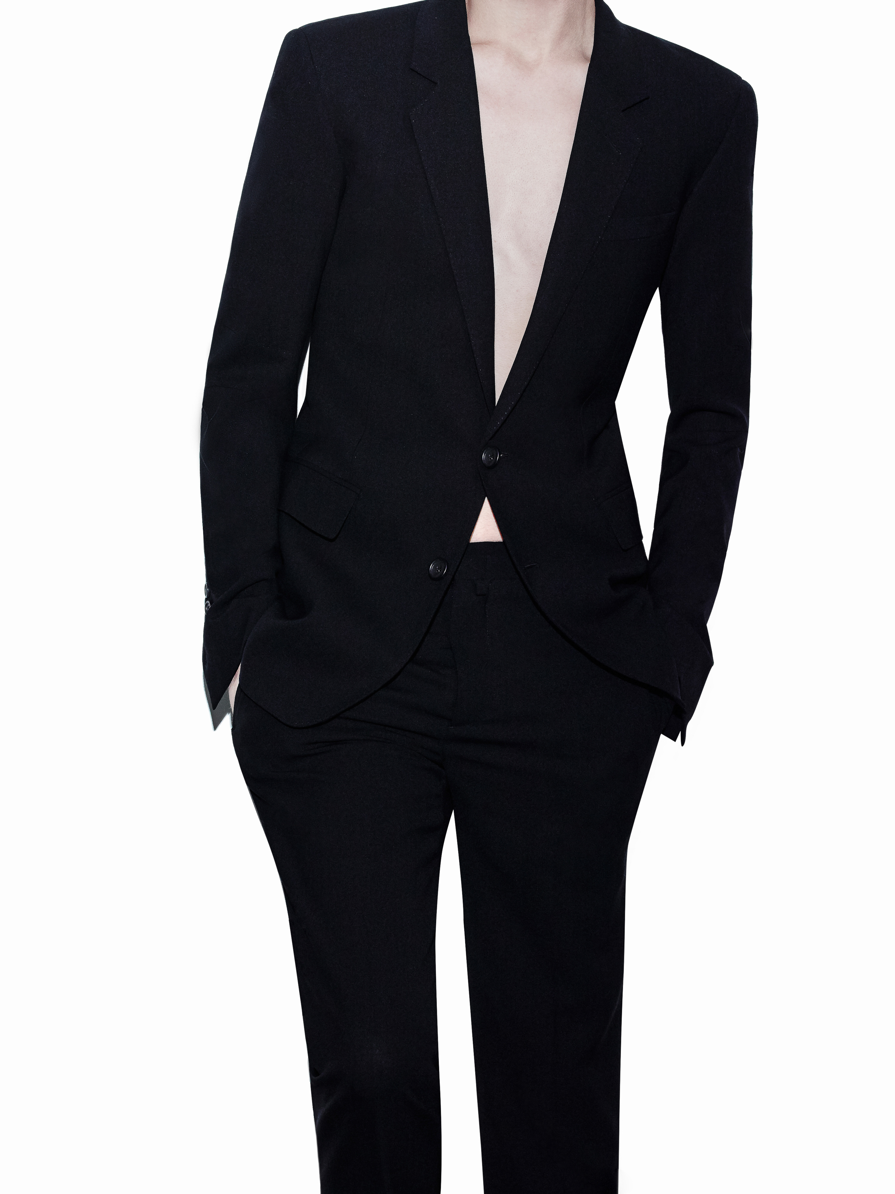 Person in black suit with hands in pockets against a white background. Fashionable, business attire for adults. Studio shot.