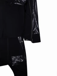 Close-up detail of black layered designer apparel featuring glossy nylon panels and zipper trims against a white seamless background.