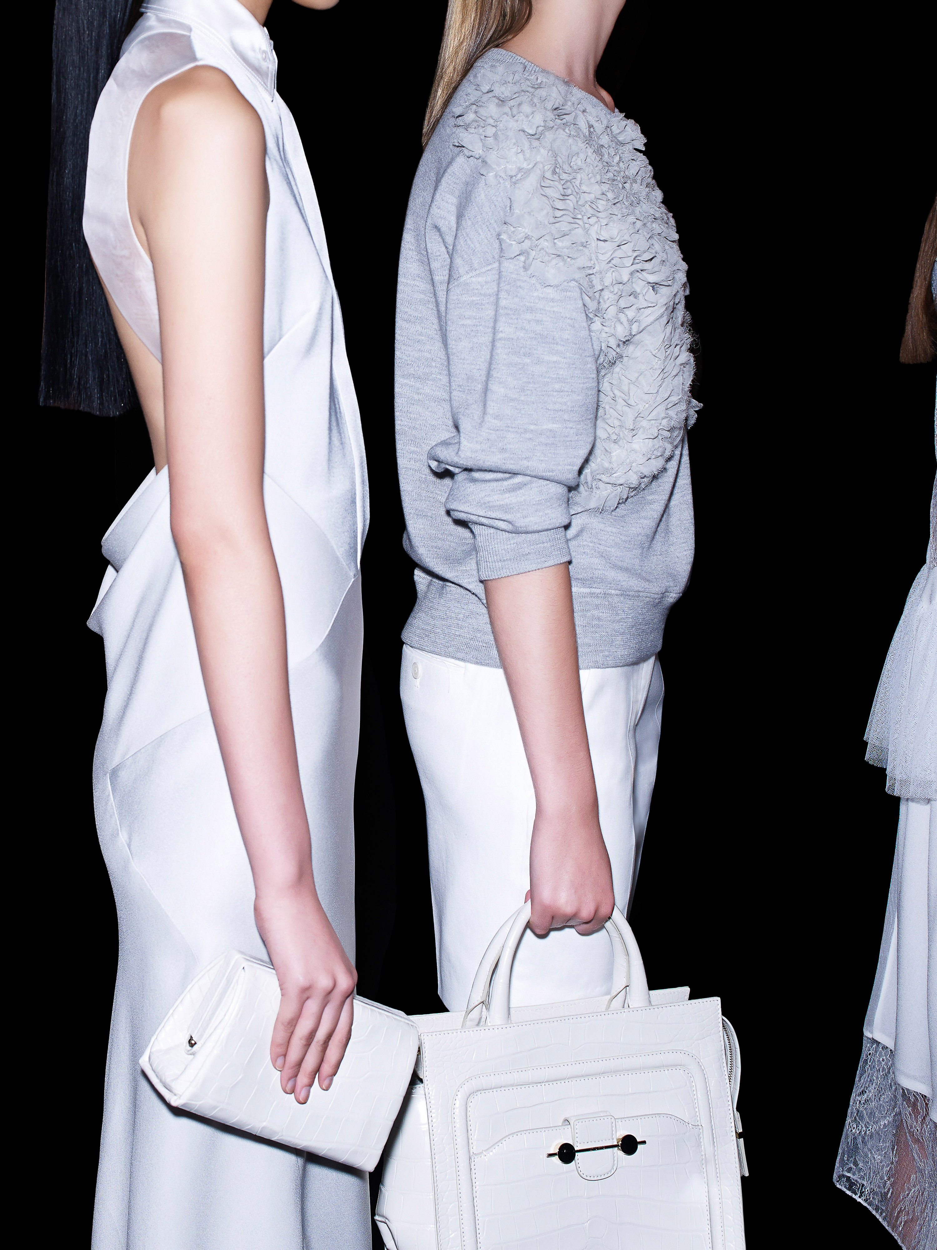 Fashion photo featuring three women in white and gray clothing. Two of the models are holding purses against a black background.