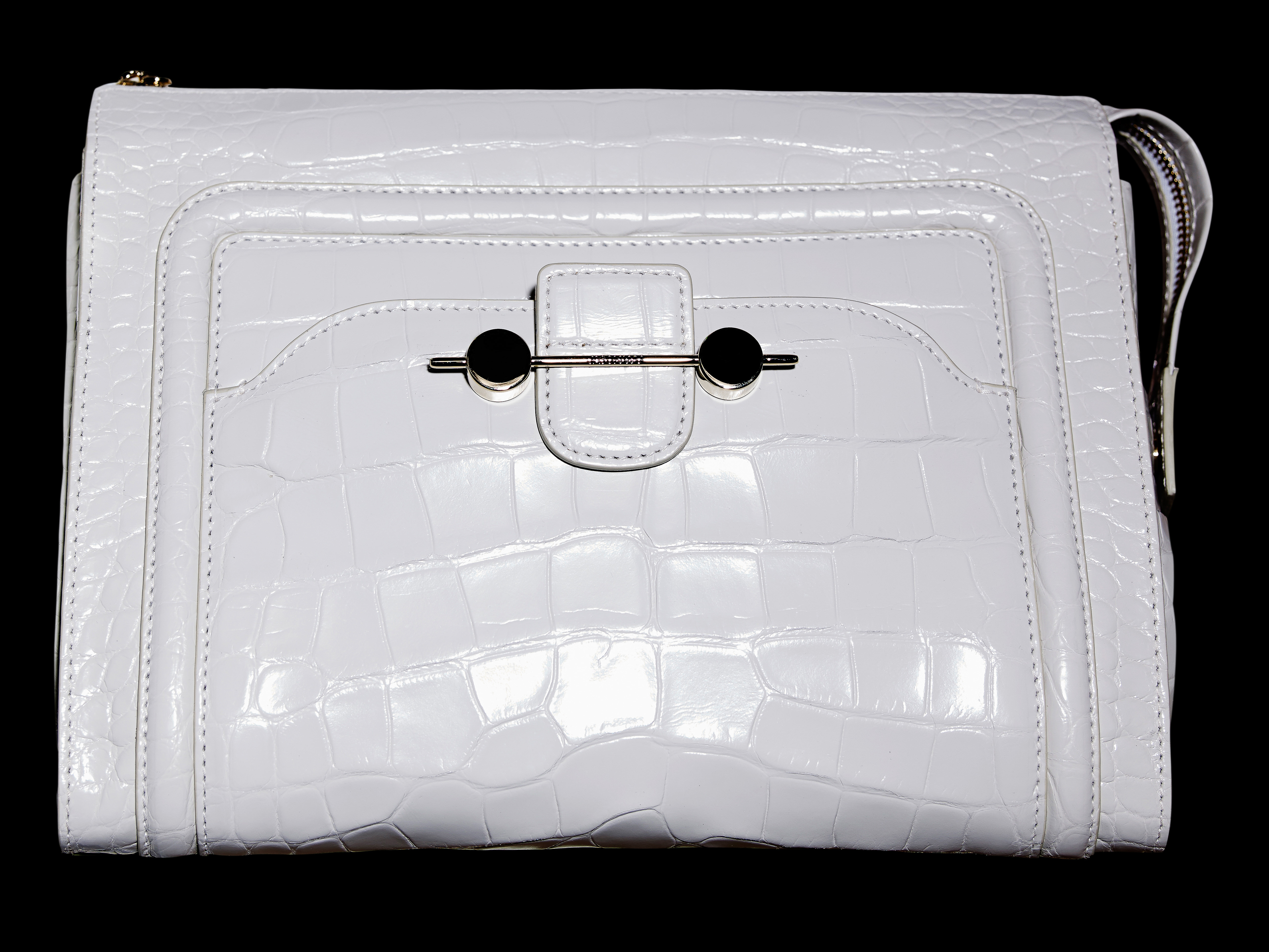 Close-up of a white handbag with a reptile-like texture. The purse has a metal clasp and black accents, set against a stark black background.