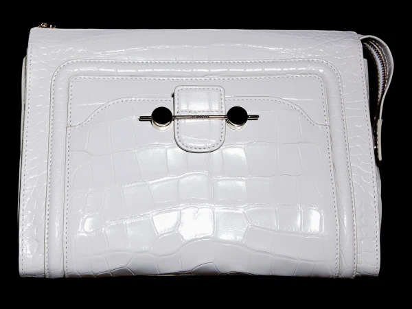 Close-up of a white handbag with a reptile-like texture. The purse has a metal clasp and black accents, set against a stark black background.