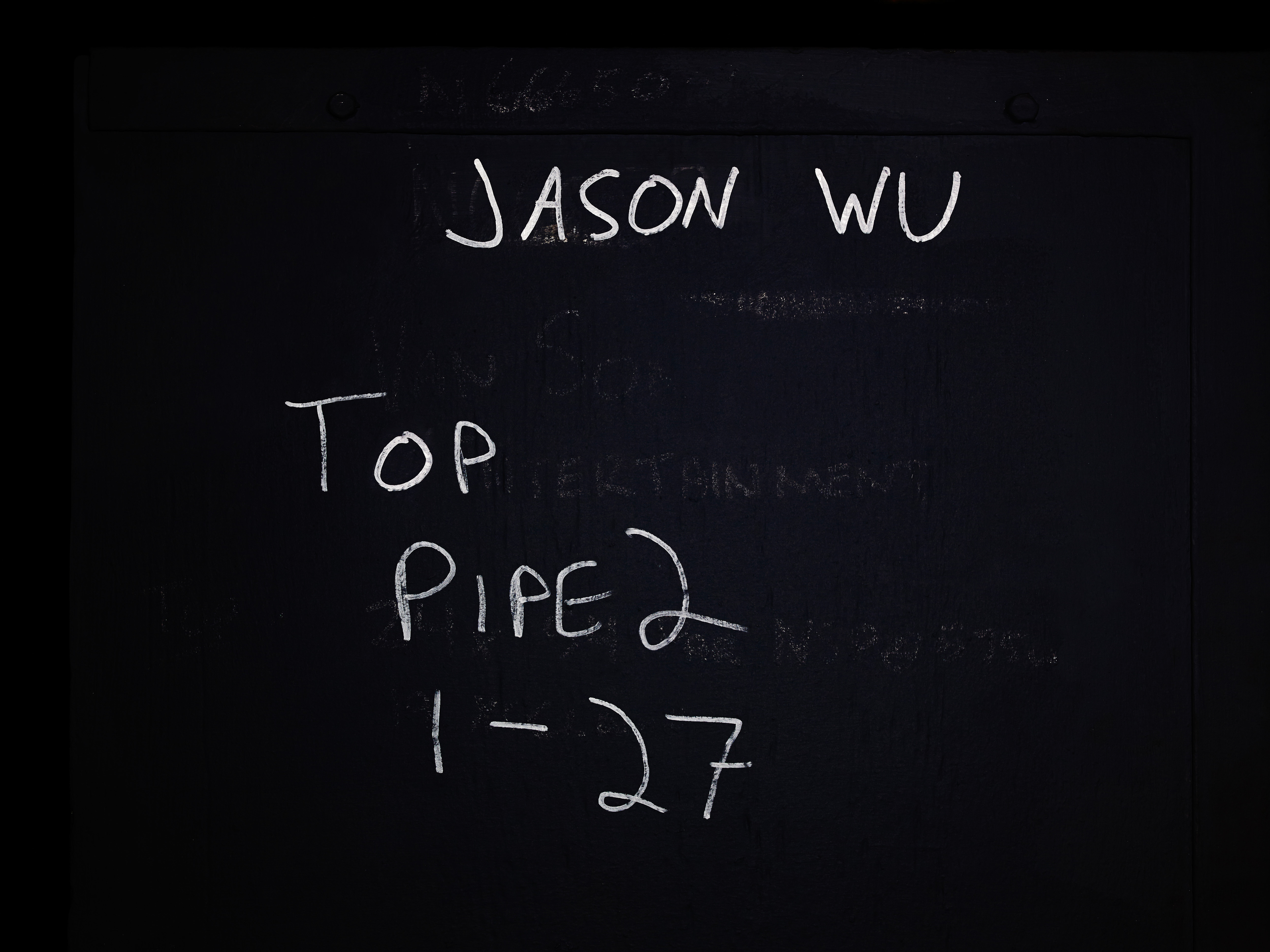 Blackboard with white handwritten text featuring 'Jason Wu,' 'Top,' 'Pipe 2,' and '1-27,' offering a stark, monochromatic visual.