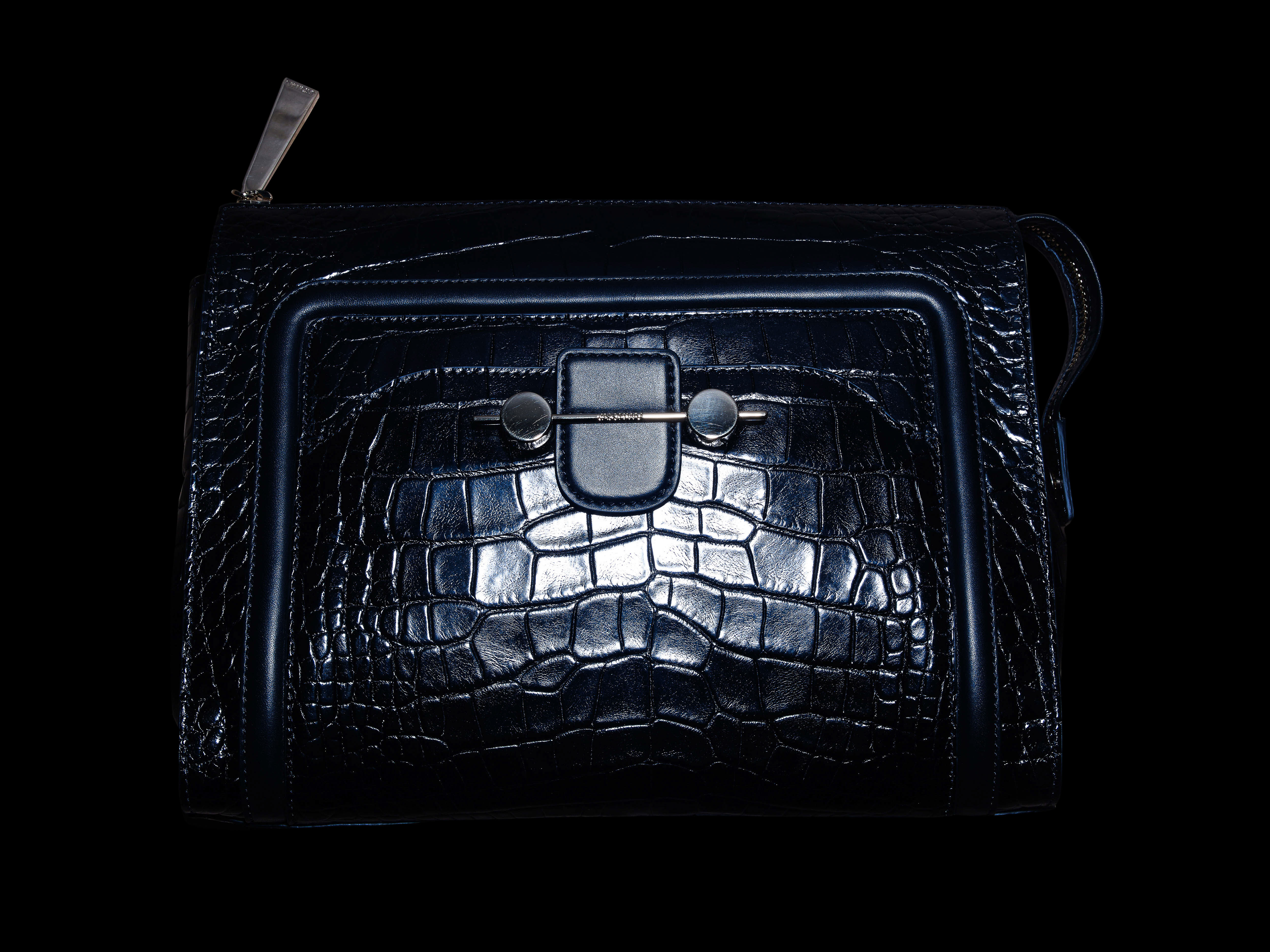 Luxury navy blue handbag made of crocodile leather with a silver clasp and zipper, set against a black studio background.