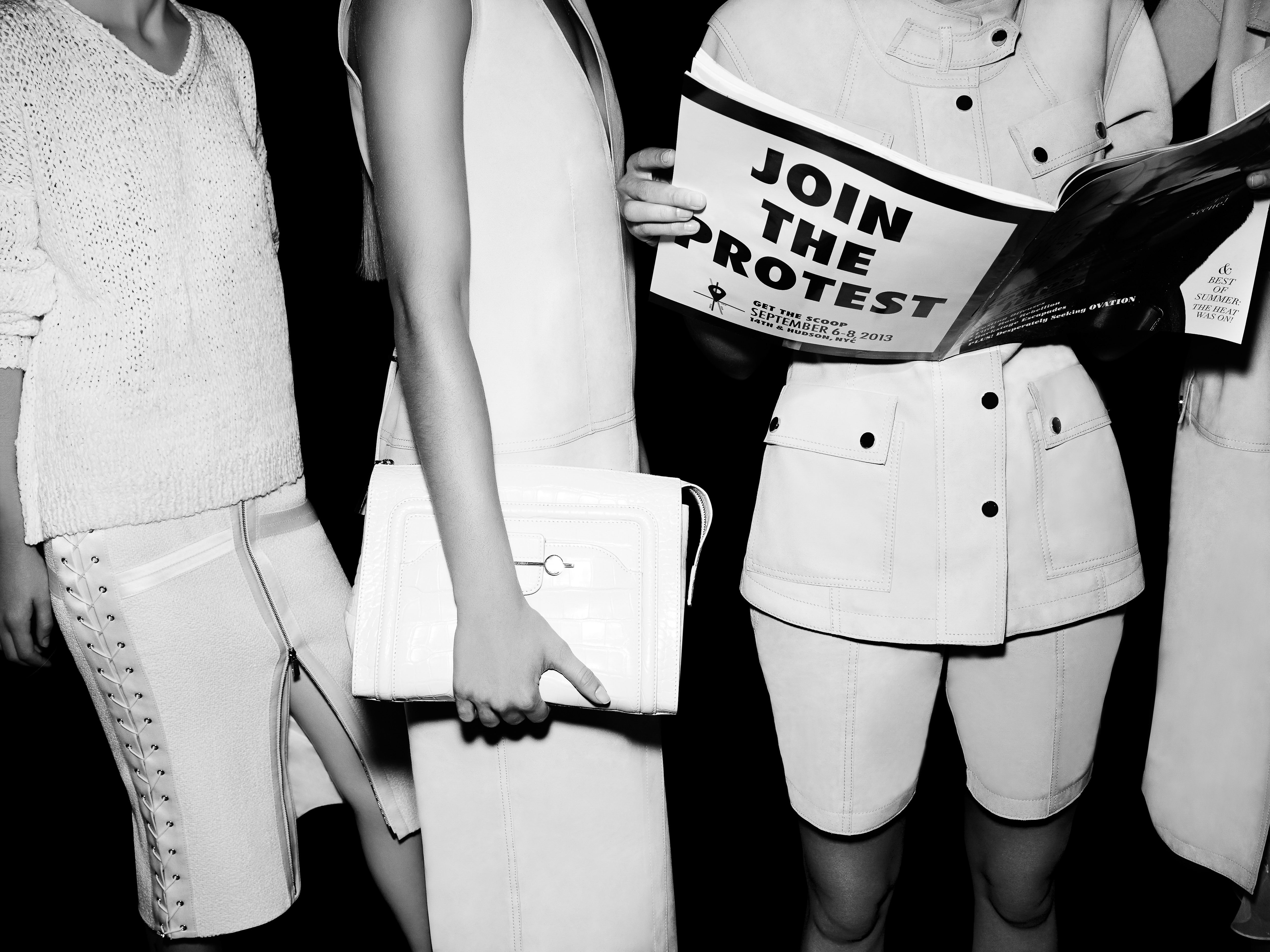 Three women in white outfits, one reading a 'Join the Protest' pamphlet in a black and white fashion editorial with high contrast.