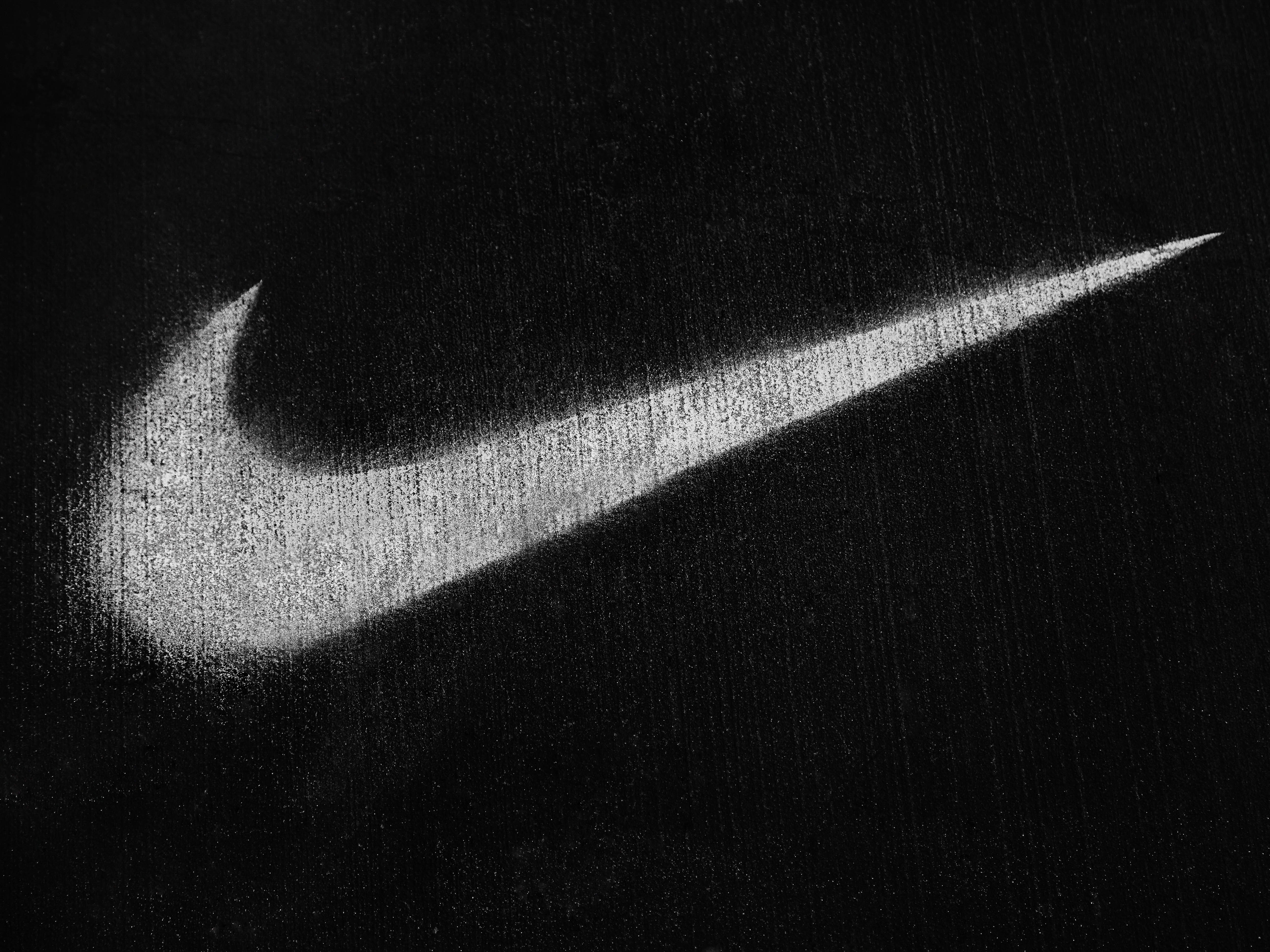 Monochromatic image of a white Nike swoosh logo painted on a dark, textured surface, conveying simplicity and brand recognition.