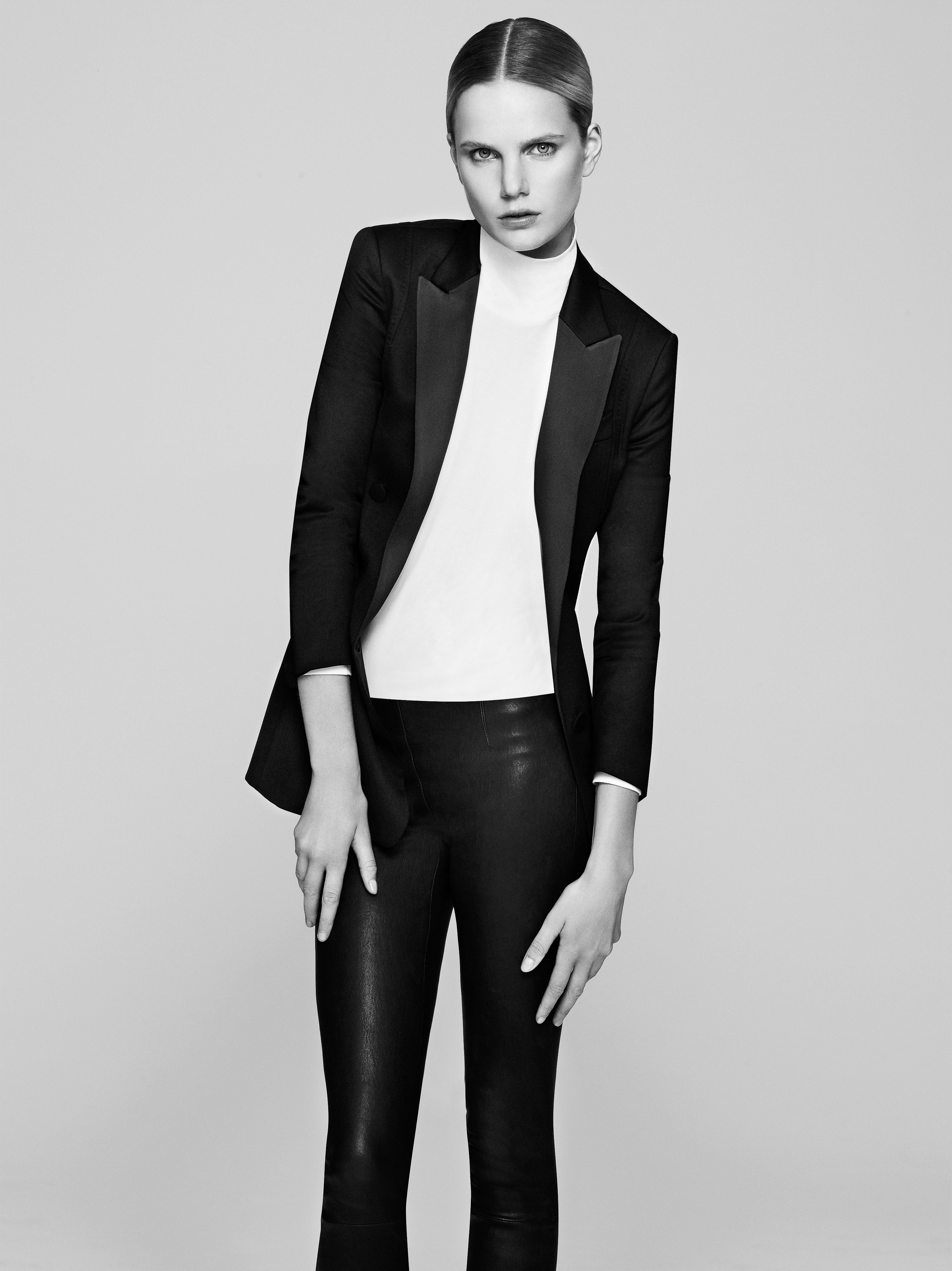 Blond woman in black blazer and leather pants poses in a studio. Fashionable portrait with a light background, clean aesthetic, and minimal makeup.