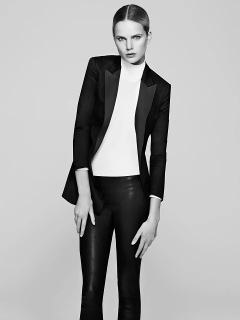 Blond woman in black blazer and leather pants poses in a studio. Fashionable portrait with a light background, clean aesthetic, and minimal makeup.