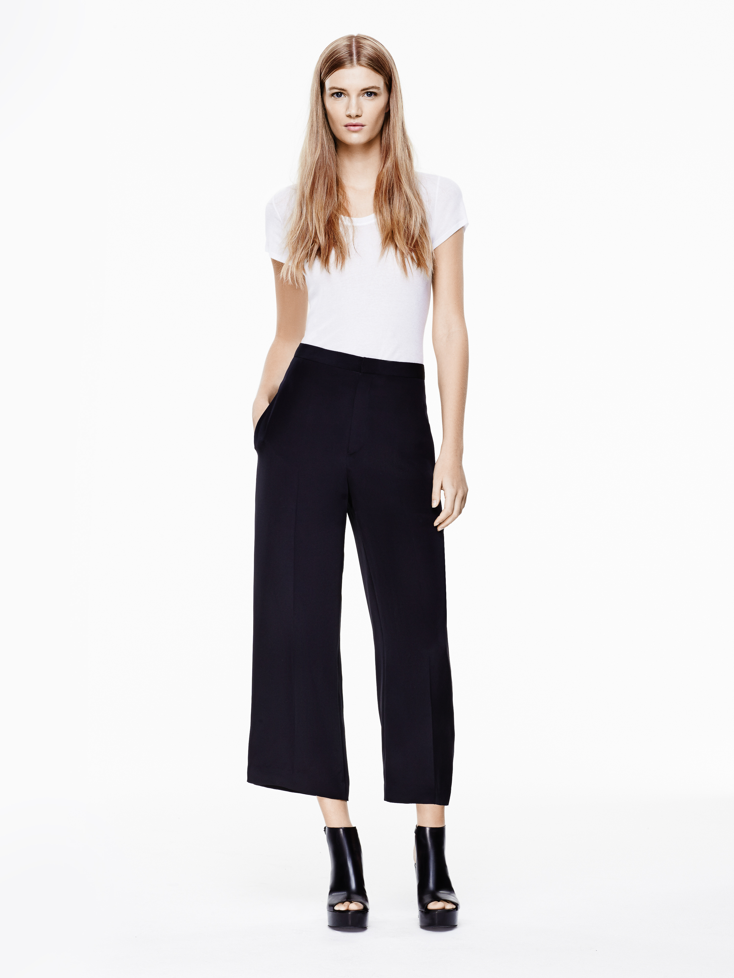 Fashion portrait of a female model wearing a white t-shirt, black culottes, and black platform sandals in a bright photo studio.
