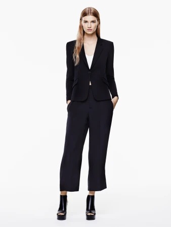 Full-length studio shot of a blonde female model in a black blazer, wide-leg pants, and platform heels on a white backdrop, fashion.