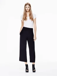 Model wearing a white t-shirt, black cropped trousers, and black platform boots against a plain white background.