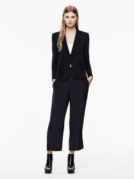 Model wearing a black blazer and matching trousers standing against a seamless white background.