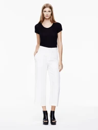 Model wearing a black short-sleeve top and high-waisted white wide-leg trousers standing against a pure white backdrop.