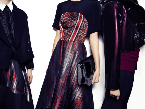 Three fashion models showcase elegant apparel with rich textures, including a jacket, dress, and skirt in a brightly lit studio setting.