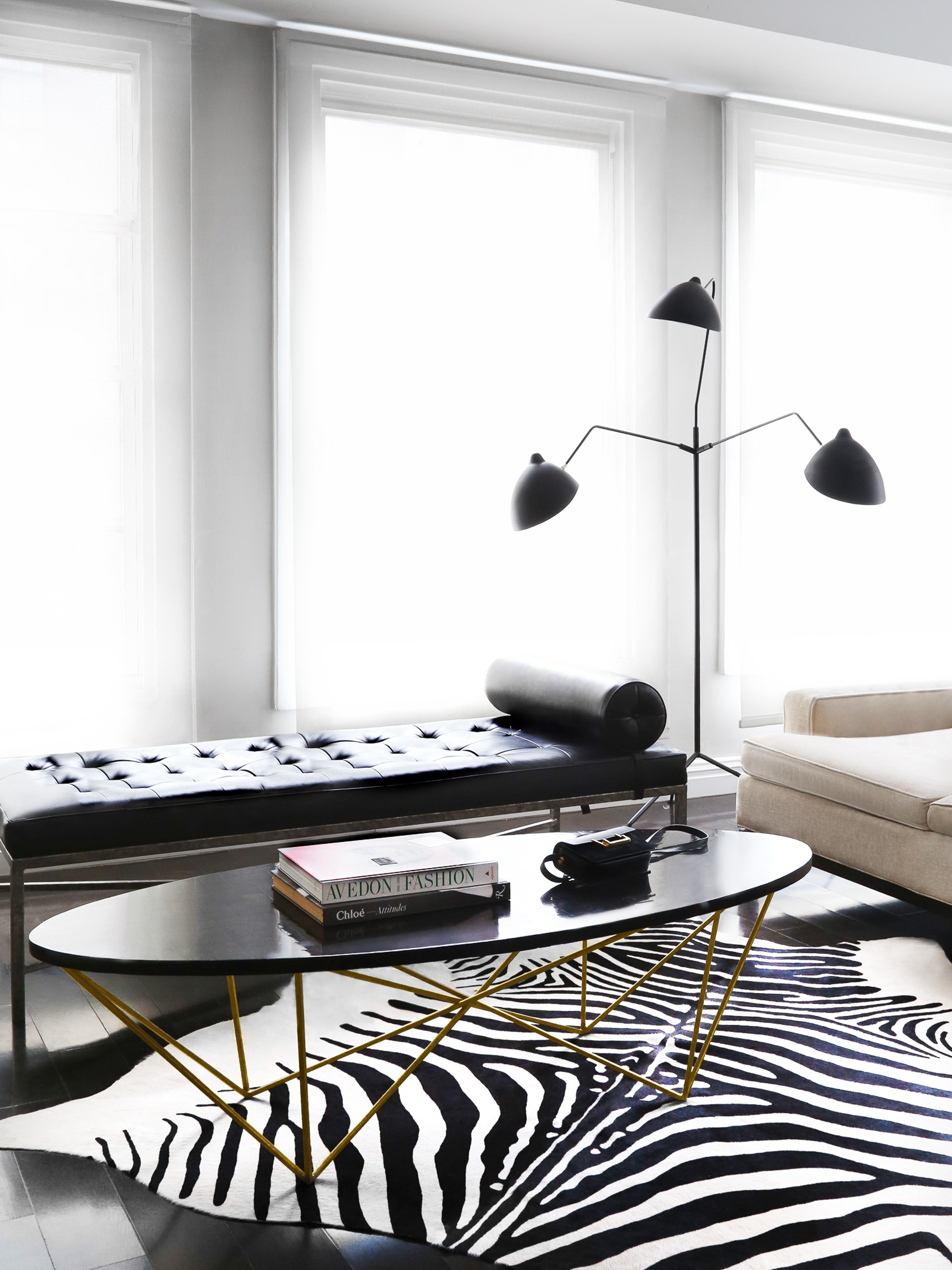 Living room interior featuring a zebra print rug, black oval coffee table with gold geometric base, and modern furniture, with natural light.