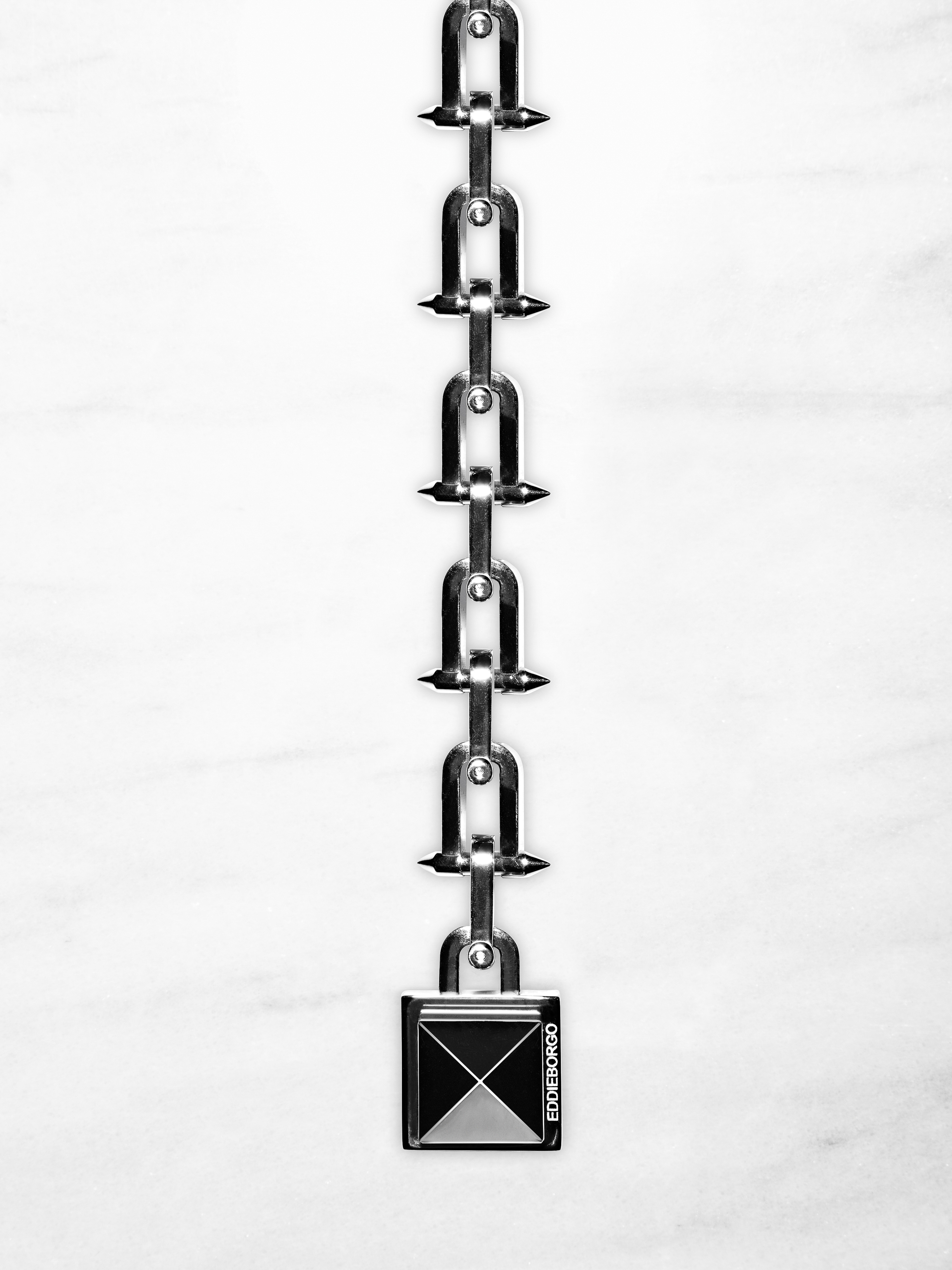 Macro shot of a shiny silver metal chain with U-shaped links and a square lock against a bright white marble background.
