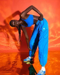 Model in blue crop top and matching track pants posing against a vibrant orange and red textured background