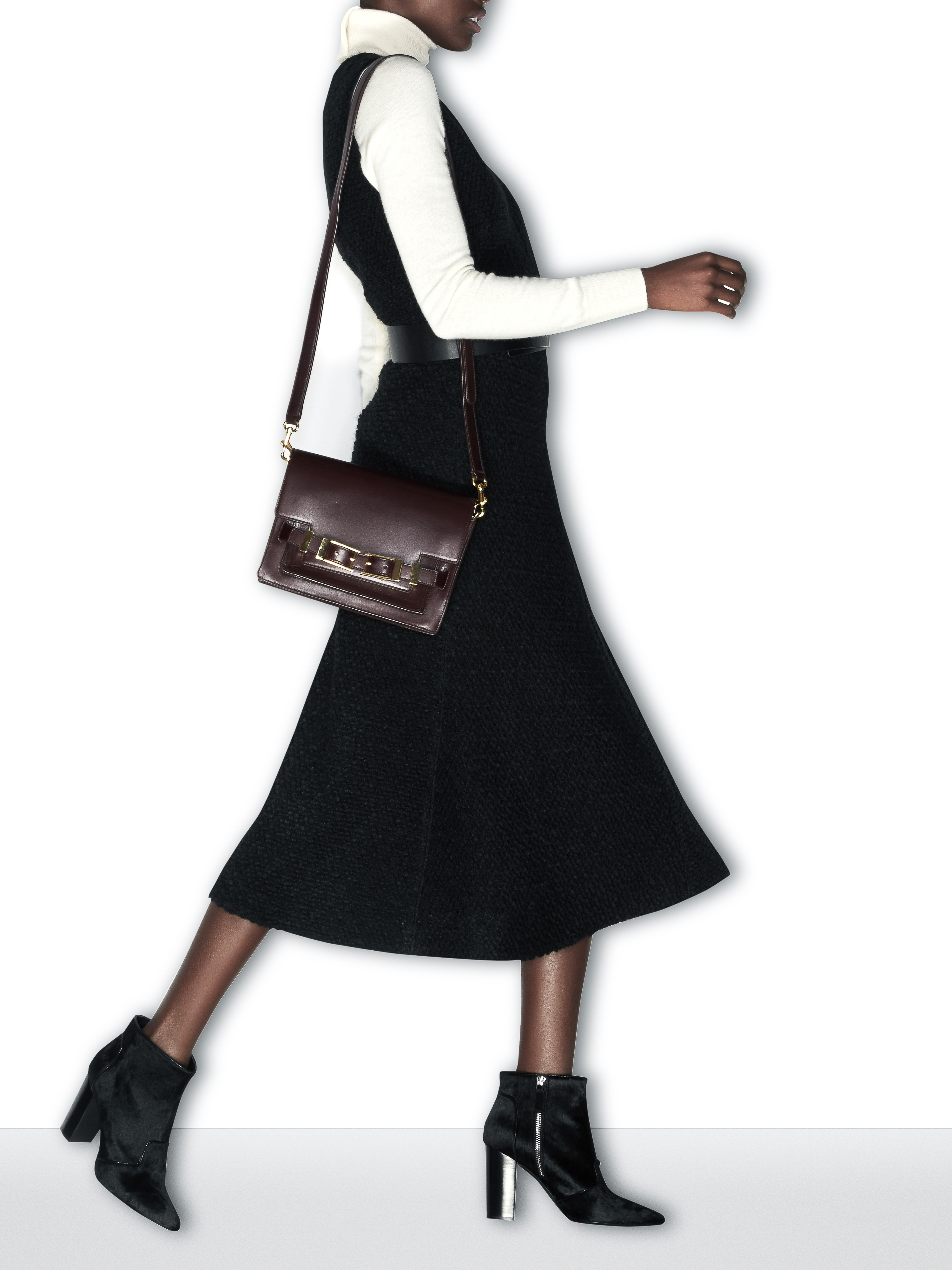 A woman walking in a black midi dress, white turtleneck, heeled ankle boots, and carrying a burgundy leather shoulder bag.