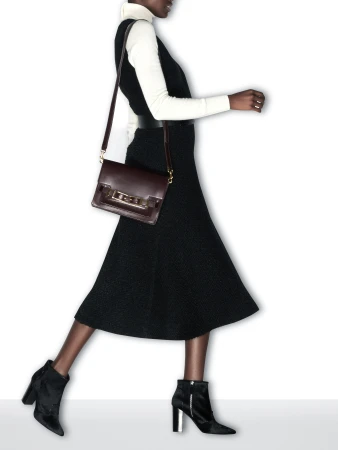 A woman walking in a black midi dress, white turtleneck, heeled ankle boots, and carrying a burgundy leather shoulder bag.