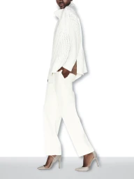 Model in profile wearing an all-white knit sweater, tailored trousers, and pointed stiletto pumps against a white studio backdrop.