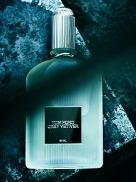 Tom Ford Grey Vetiver fragrance bottle in frosted fluted glass with a ribbed silver cap set on a textured stone surface.