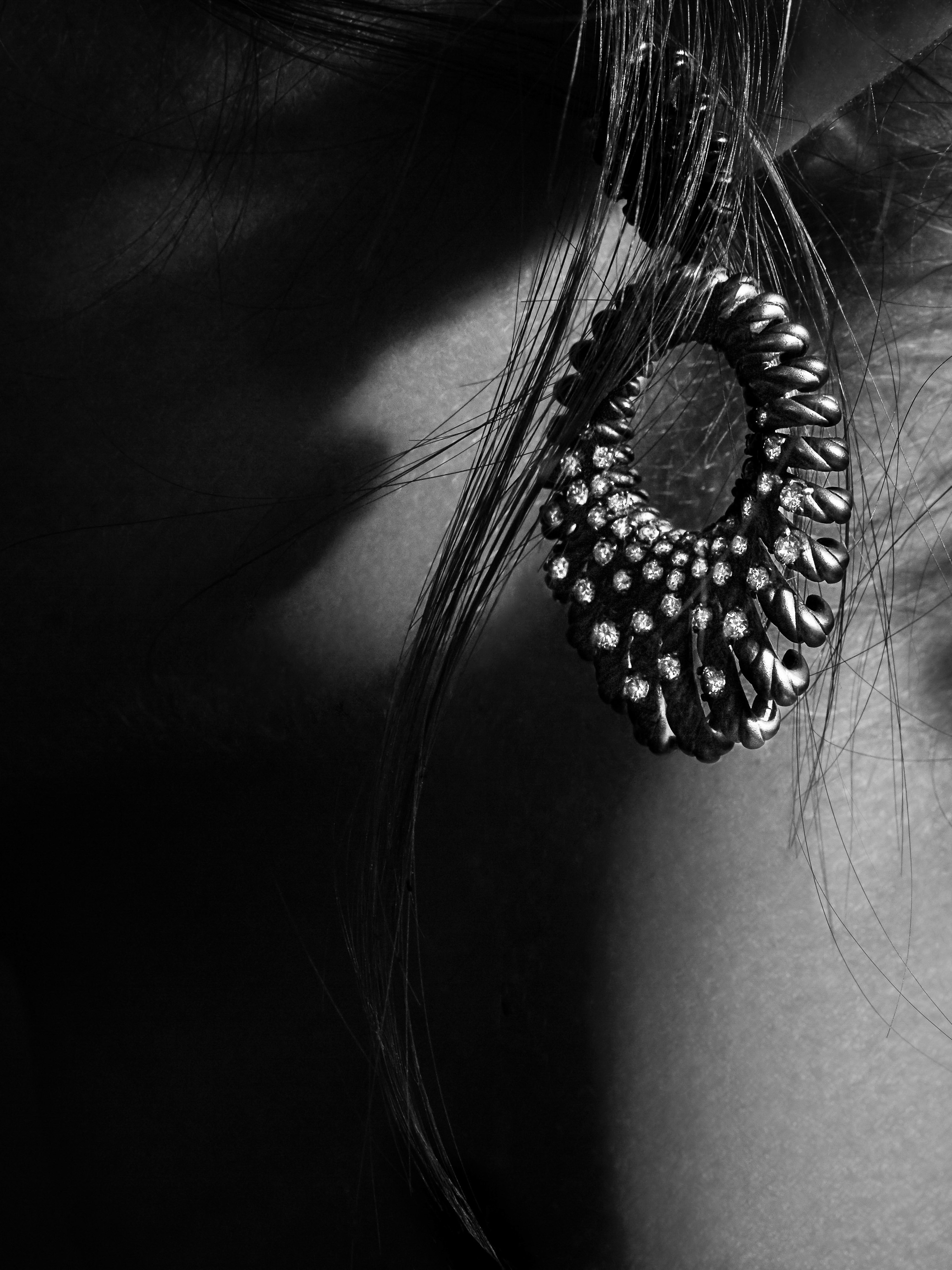 Close-up black and white shot of a woman's ear with a large, ornate dangling earring featuring intricate designs and small stones.
