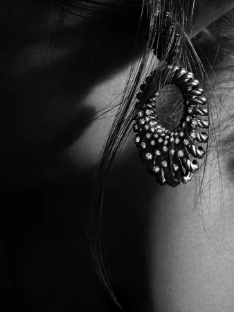Close-up black and white shot of a woman's ear with a large, ornate dangling earring featuring intricate designs and small stones.