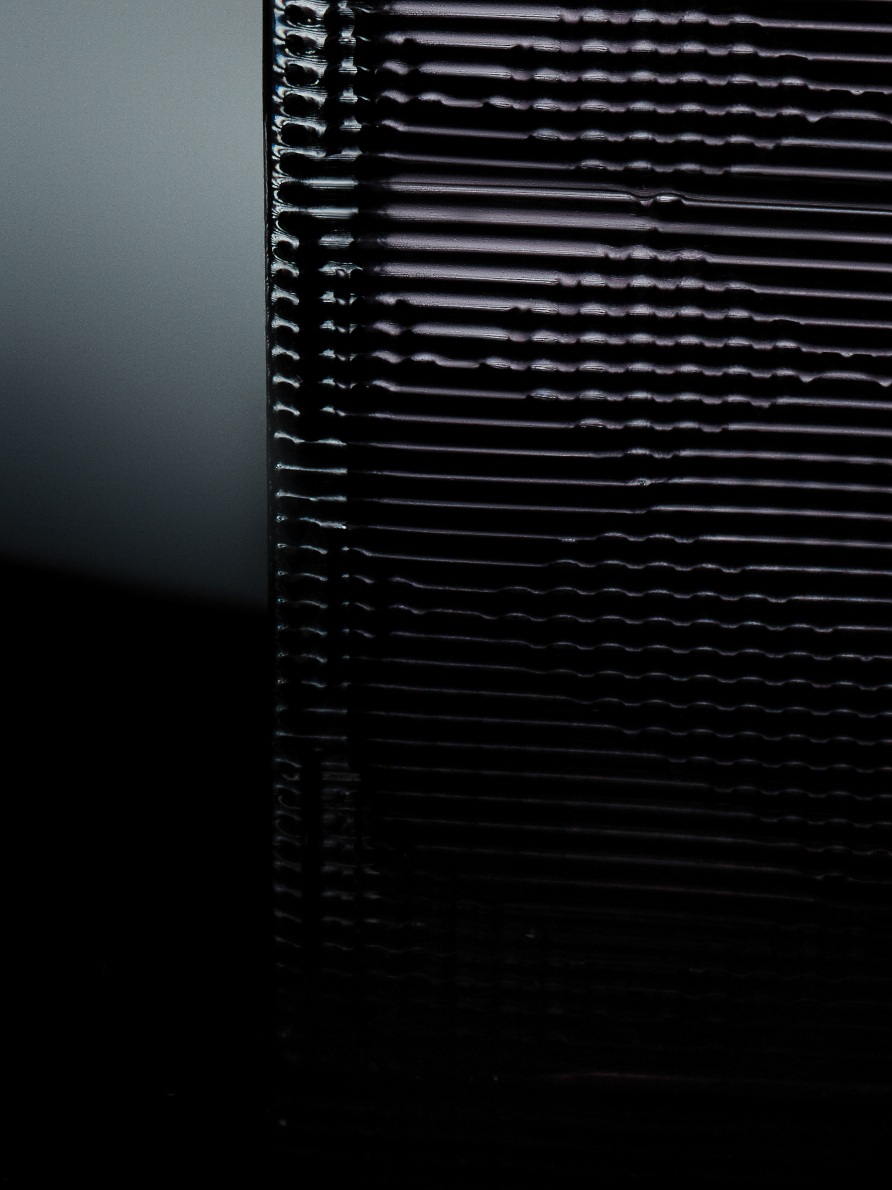 Extreme close-up of a black textured surface with horizontal lines, creating a dark, abstract pattern with subtle light reflections.