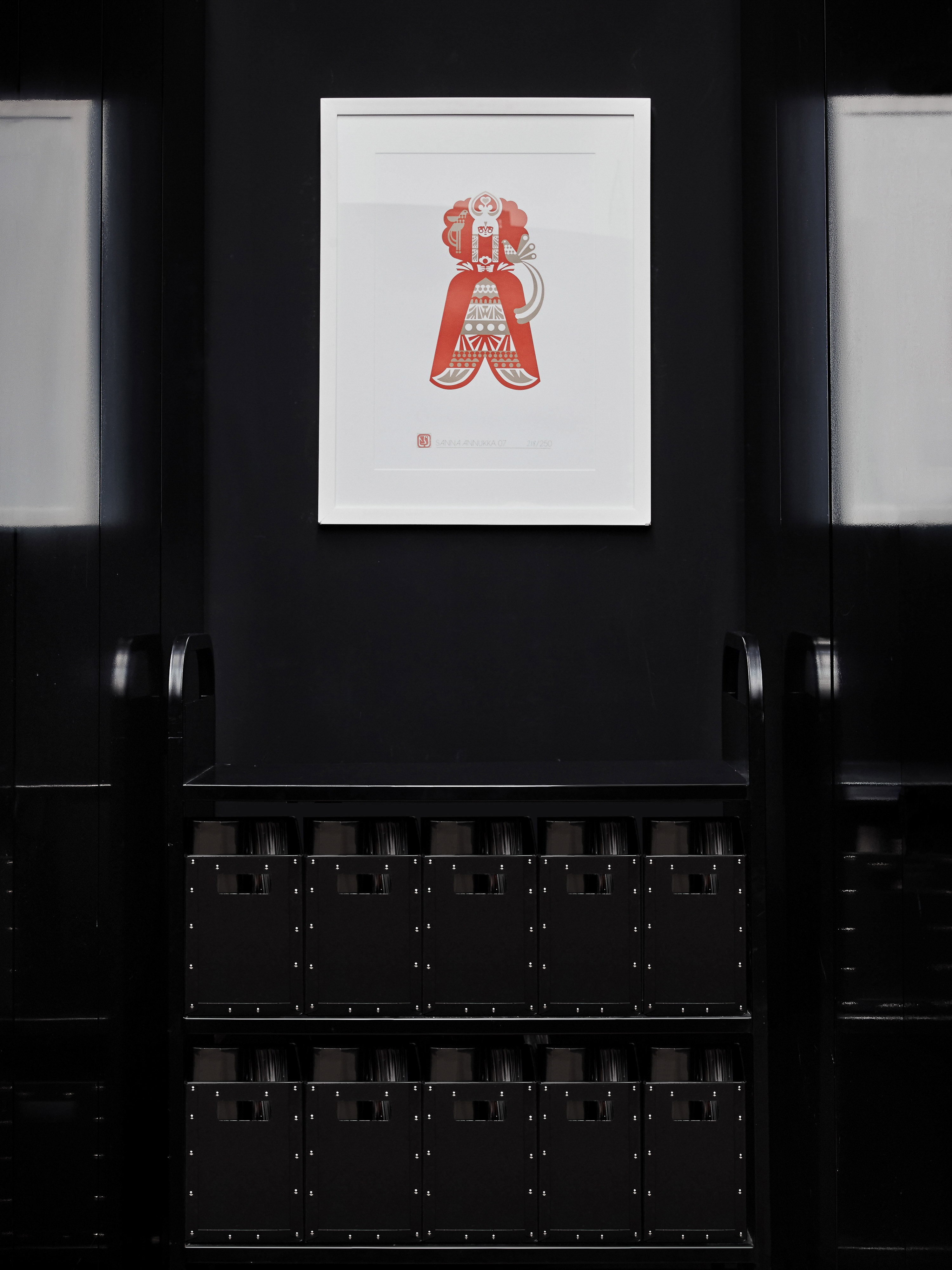 Artwork in a white frame hangs on a black wall above two stacked rows of black, rectangular containers with small square cutouts.