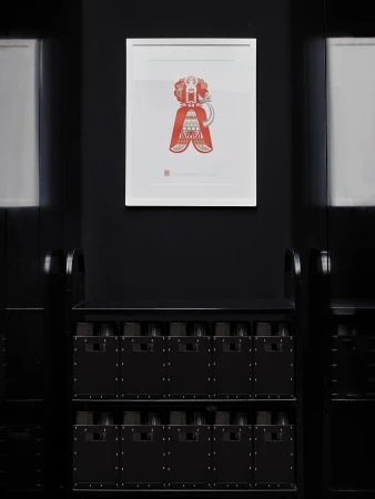 Artwork in a white frame hangs on a black wall above two stacked rows of black, rectangular containers with small square cutouts.