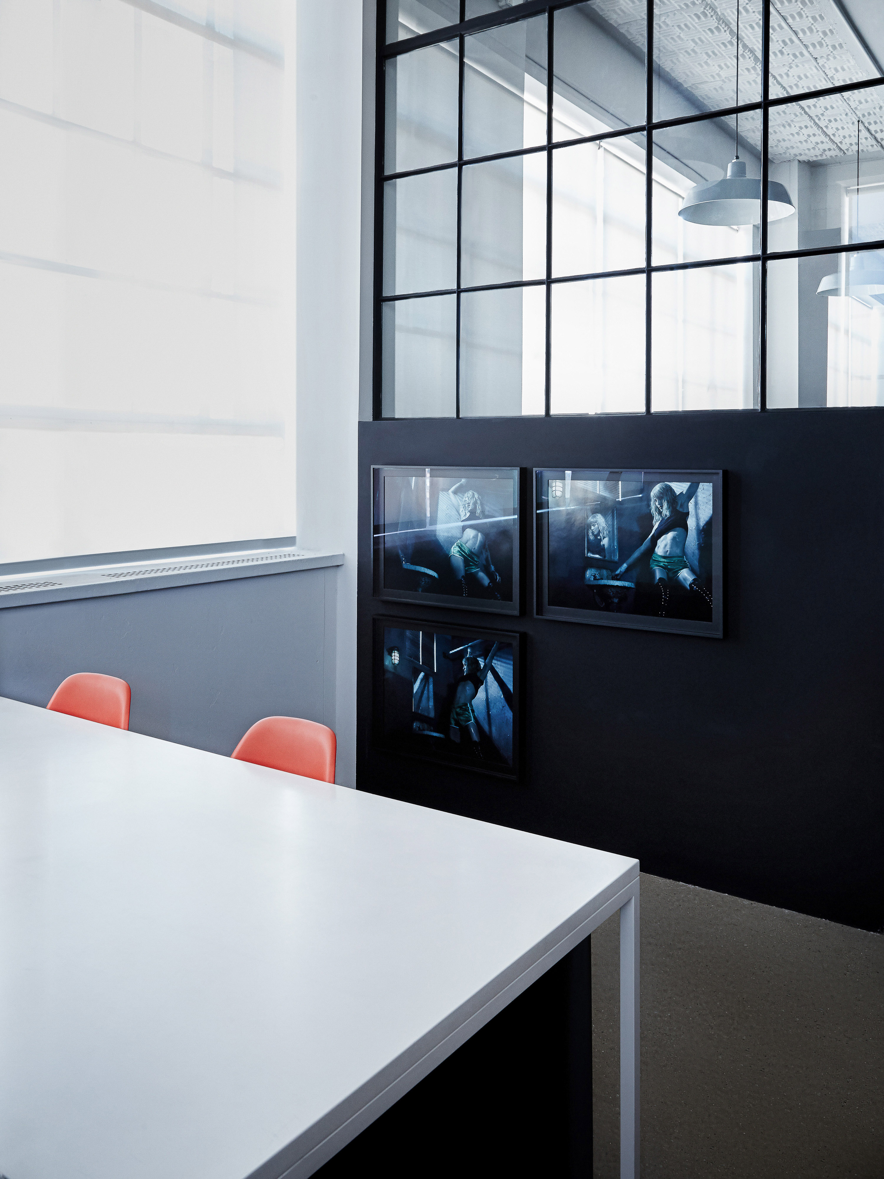 Conference room interior with a long white table, orange chairs, and framed art on a dark grey wall with a large black-framed window.