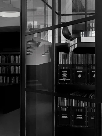 Black and white photo of a modern interior with books on shelves, hanging pendant lights, and reflections in glass panels.