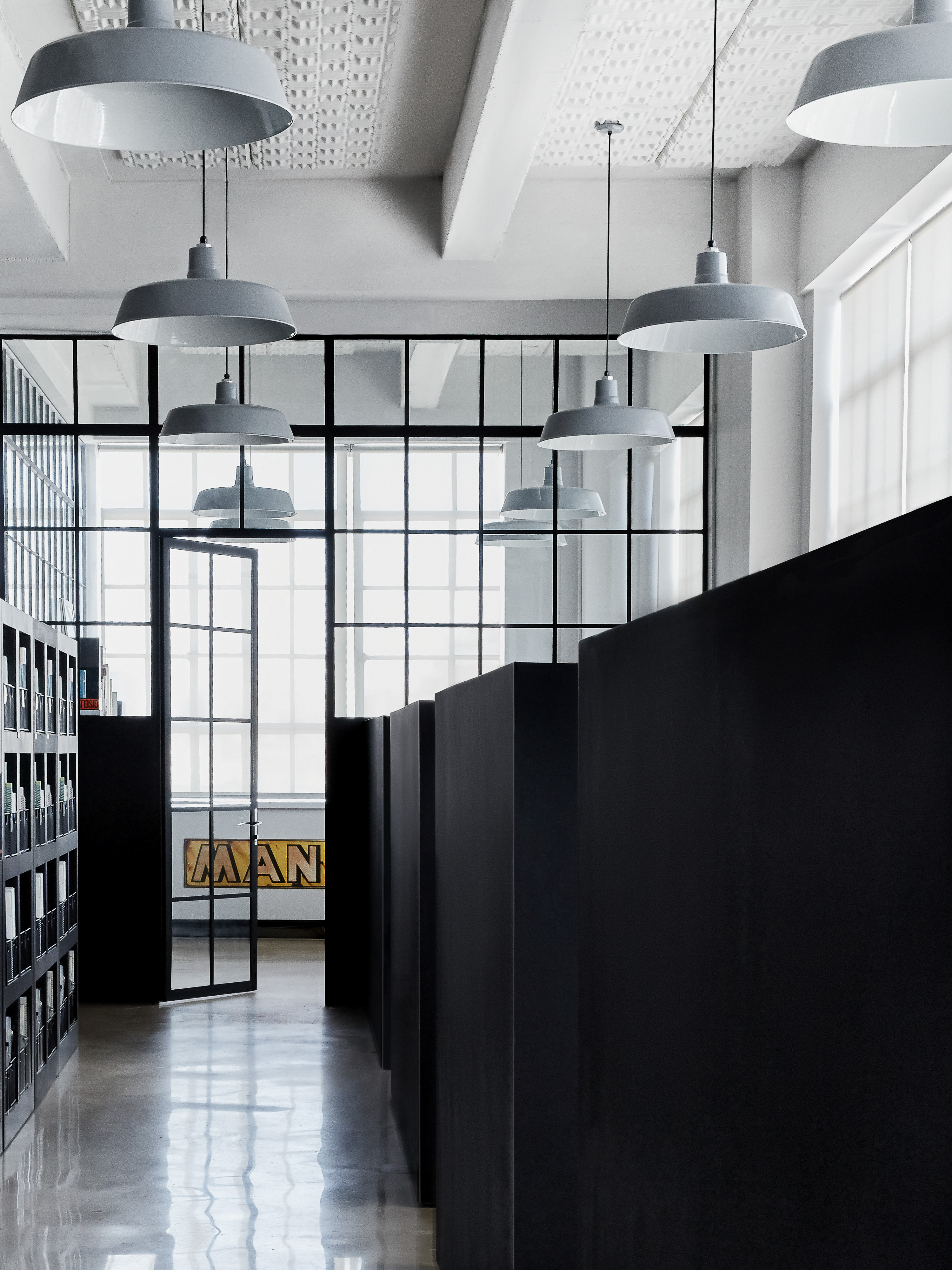 Interior view of a modern reading room with black shelves and desks, gray pendant lights, and a black-framed glass wall.