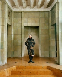 Luna Wedler poses in a dark printed jacket and black knee-high boots in a green and ochre tiled hall for Vogue Germany.