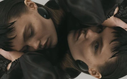 Close-up portrait of model Kiki Jewel resting on her reflection wearing large black oval earrings and a black jacket.