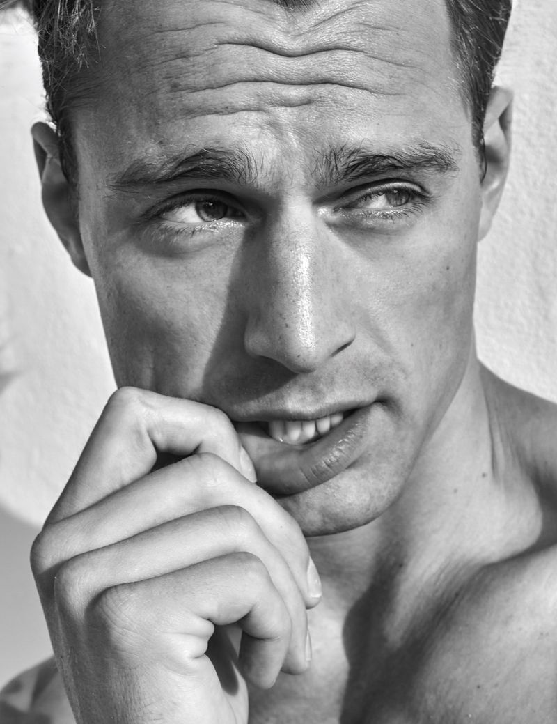 Black and white portrait of a handsome adult male with hand near face, looking off to the side against a solid neutral background.