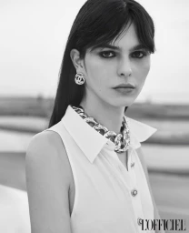 Monochrome fashion portrait of a model wearing a white sleeveless shirt, chunky chain necklace, and logo earrings.