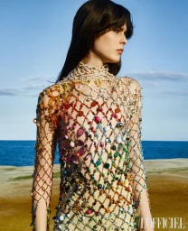 Model Julia Meseguer wearing an intricate multicolored beaded net garment against an ocean backdrop for L'Officiel Ukraine.