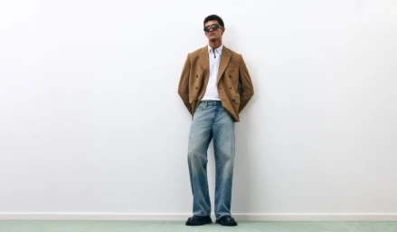 Model Bodhi Heeck wearing a camel blazer, white shirt, light wash jeans, and sunglasses against a minimal white wall.