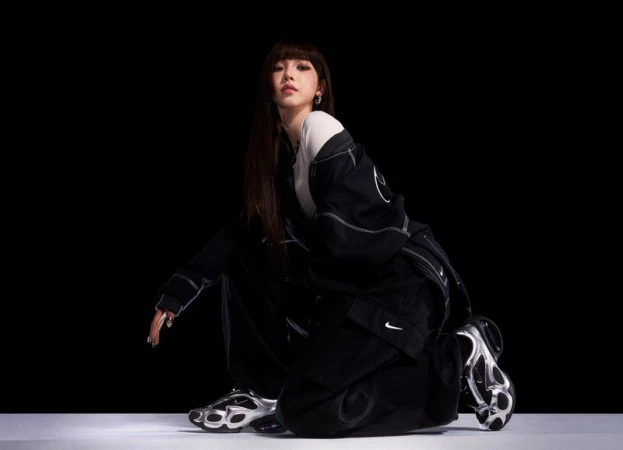Model crouching in a black Nike tracksuit and metallic silver sneakers against a dark studio background.