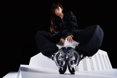 Karina of aespa poses in an oversized black outfit and metallic silver Nike Air Max sneakers on a white geometric platform.