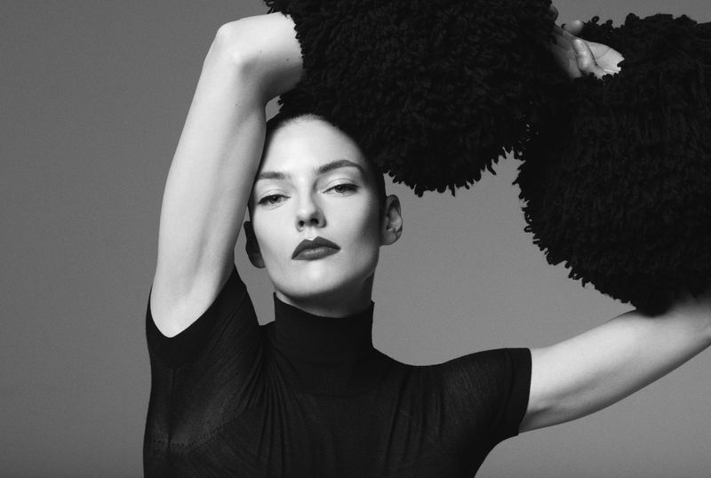 Elegant studio portrait of a woman in a black turtleneck with an avant-garde textured black scarf, captured in a high-contrast black and white shot.