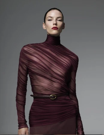 Model Beauïse Genç wearing a ruched sheer burgundy high-neck top with a thin belt against a neutral grey studio backdrop.