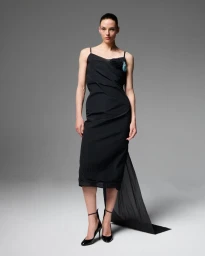 Model wearing a black spaghetti strap dress with a long train standing against a plain grey studio backdrop.