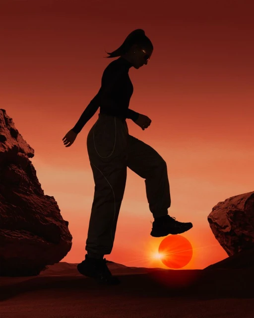 Silhouette of a woman stepping between two rocks with a sunset/sunrise in the background, creating a dramatic landscape.