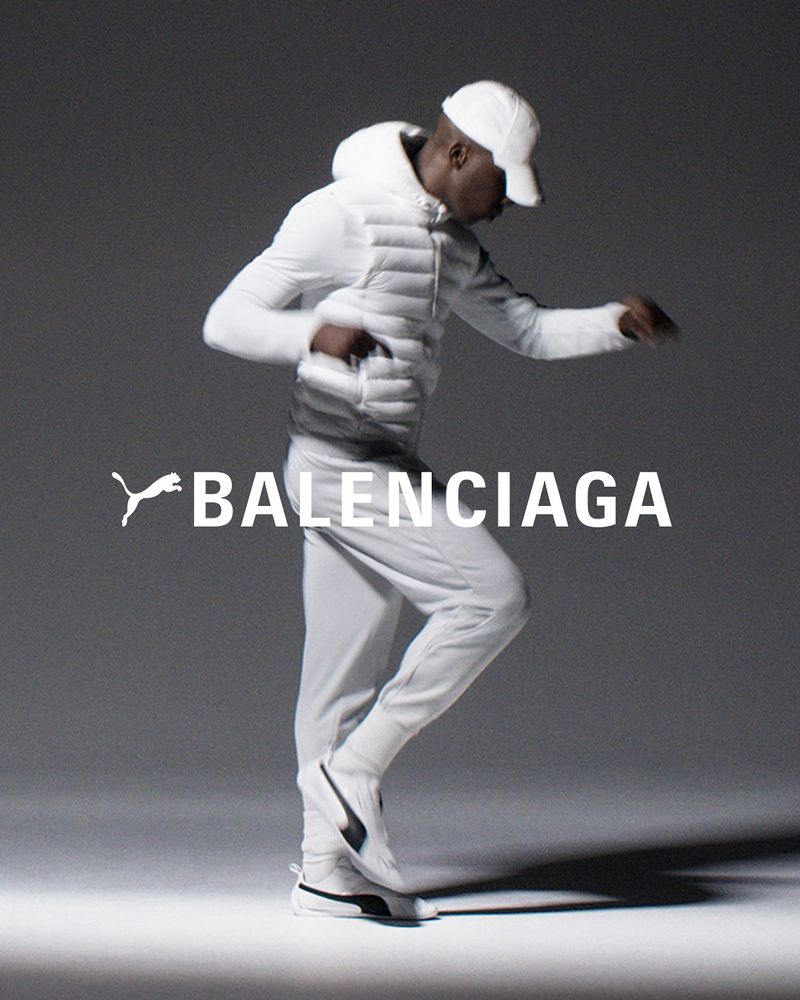 An African-American male model in white sportswear strikes a dynamic pose in a studio fashion shot for Puma x Balenciaga collaboration.