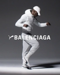 Man in white hooded jacket, sweatpants, and cap dynamic posing against a dark studio background for Balenciaga x Puma.
