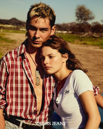 Fashion image of a young adult couple outdoors, wearing casual clothing. The man wears a plaid shirt, and the woman a white top.