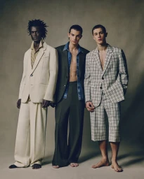Three male models in tailored suits standing barefoot against a neutral studio background for Ami Paris SS25 campaign