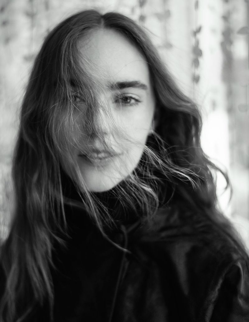 Black and white portrait of a young woman with long hair partially obscuring her face, wearing a black turtleneck sweater.